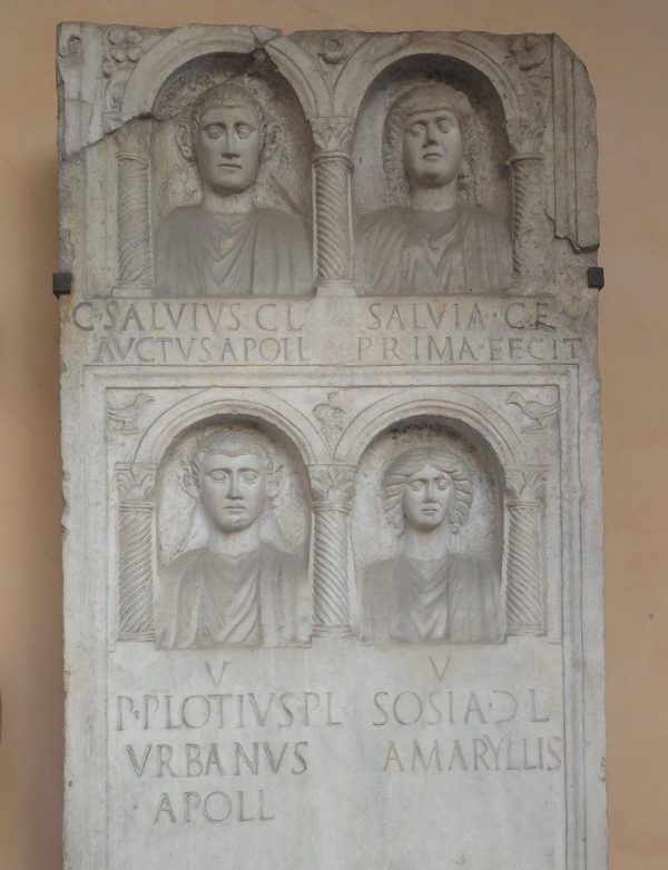 Roman gravestone showing four faces (two male, two female), each with an inscription giving the dead person's name.